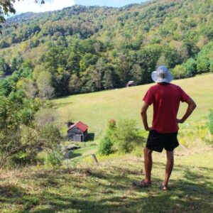 man from the back looking down at barn and field and mountains