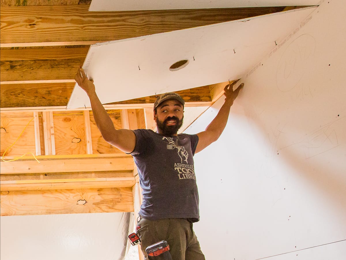 Instructor Keenan Thompson demonstrating how to install drywall on a ceiling of a DIY Tiny House constructed during a Wild Abundance Workshop