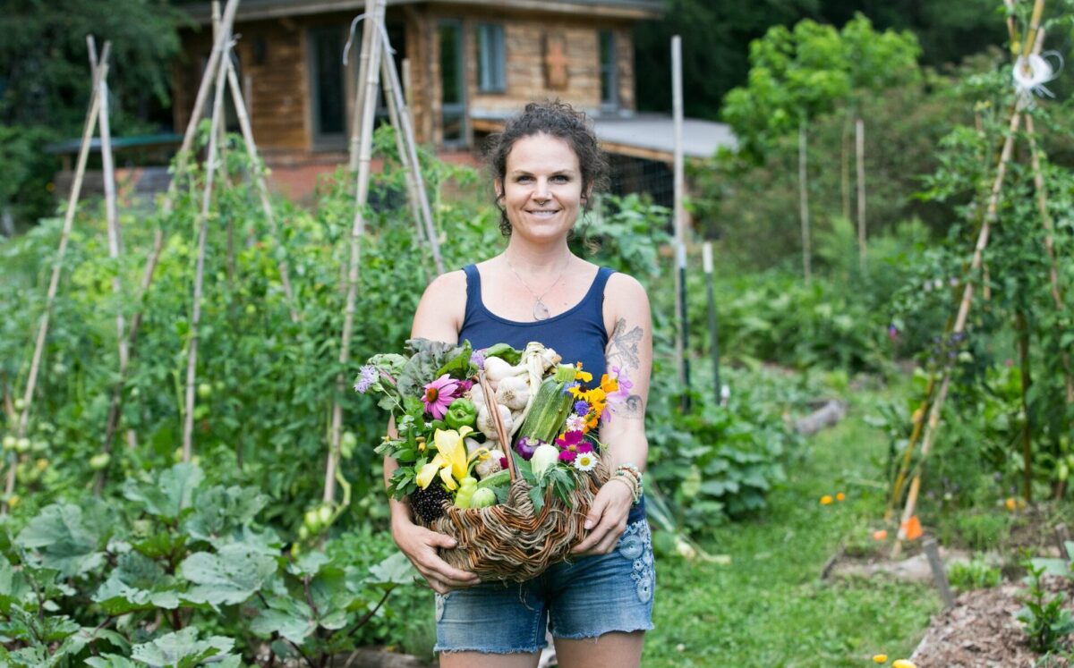 A gardening and permaculture apprentice smiles showing her basket of harvested vegetables from the garden at wild abundance