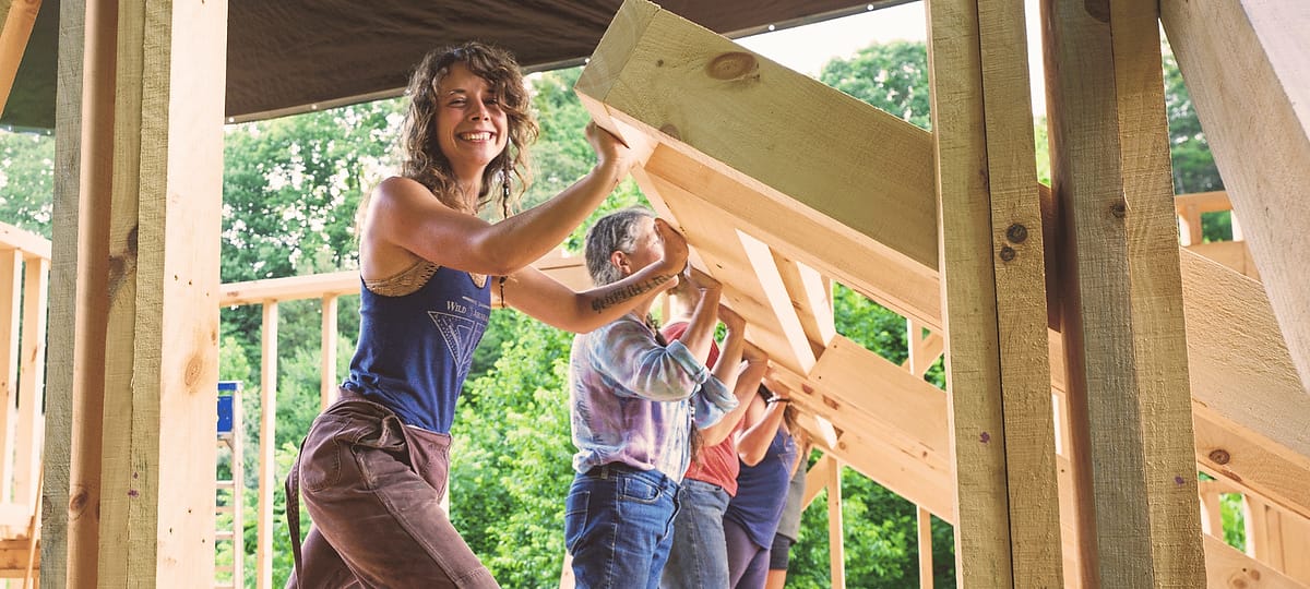 A woman smiles at the camera as she and her friends raise the first wall of her DIY Tiny House build