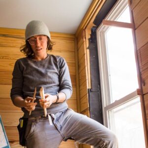 woman installing a salvaged window while building a tiny house