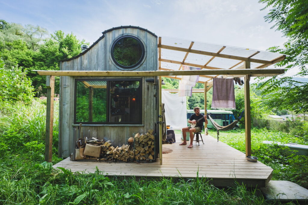 A man plays banjo on the porch of his tiny home.