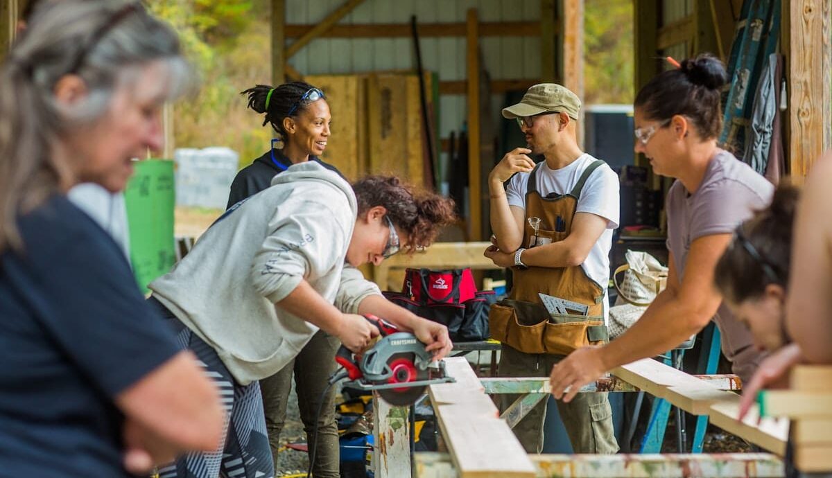 students smile while taking turns practicing cutting boards with the circular saw in a carpentry workshop for adults at Wild Abundance