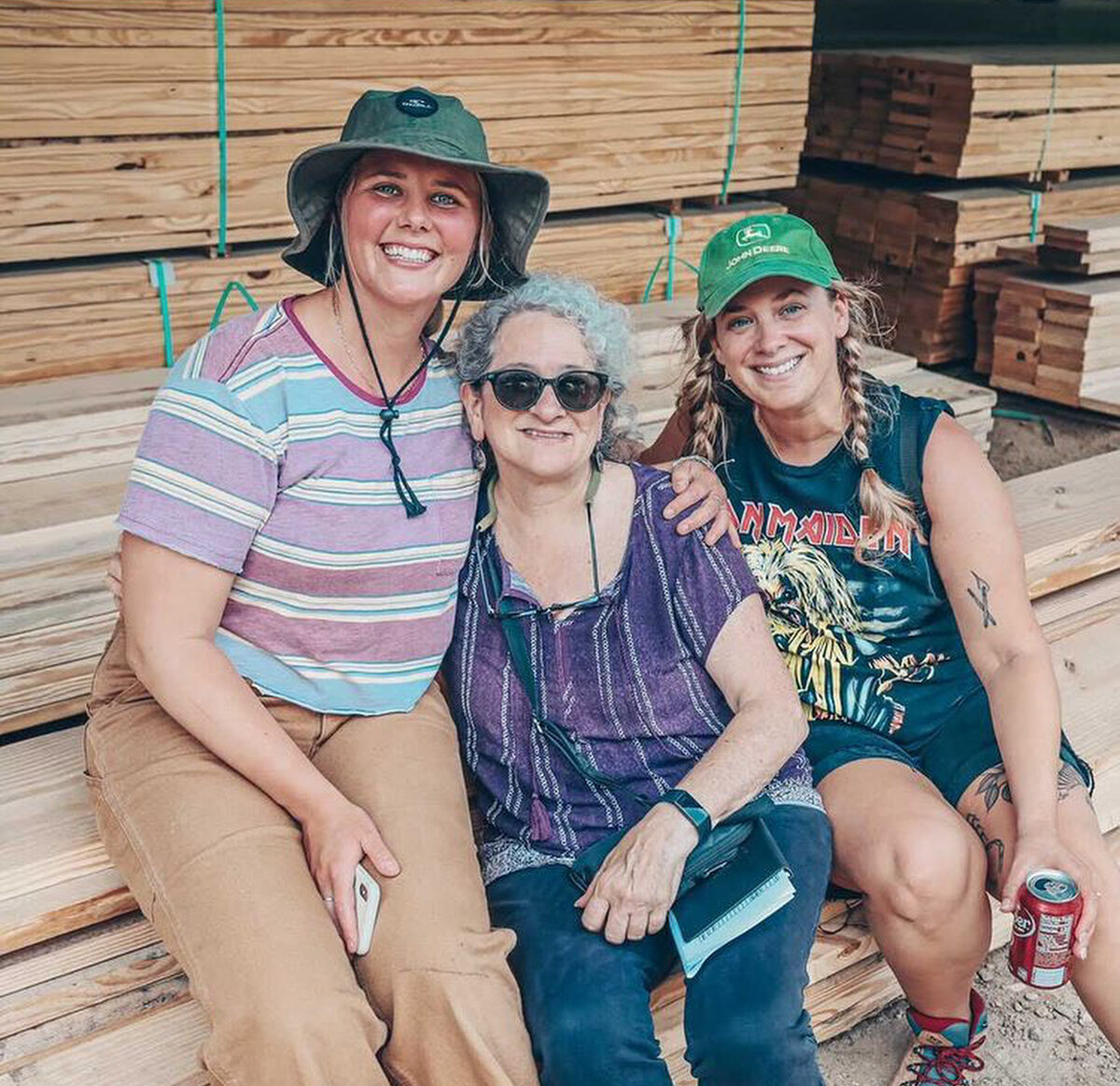 3 women smile for a group picture at the lumber yard during a field trip to practice selecting wood suitable for a carpentry project during a women's basic carpentry class at Wild Abundance