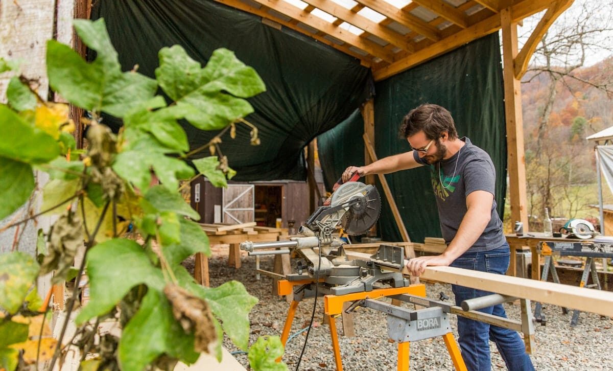 A man practicing cutting boards to length on a miter saw during an Adult Basic Carpentry 4 day bootcamp at Wild Abundance