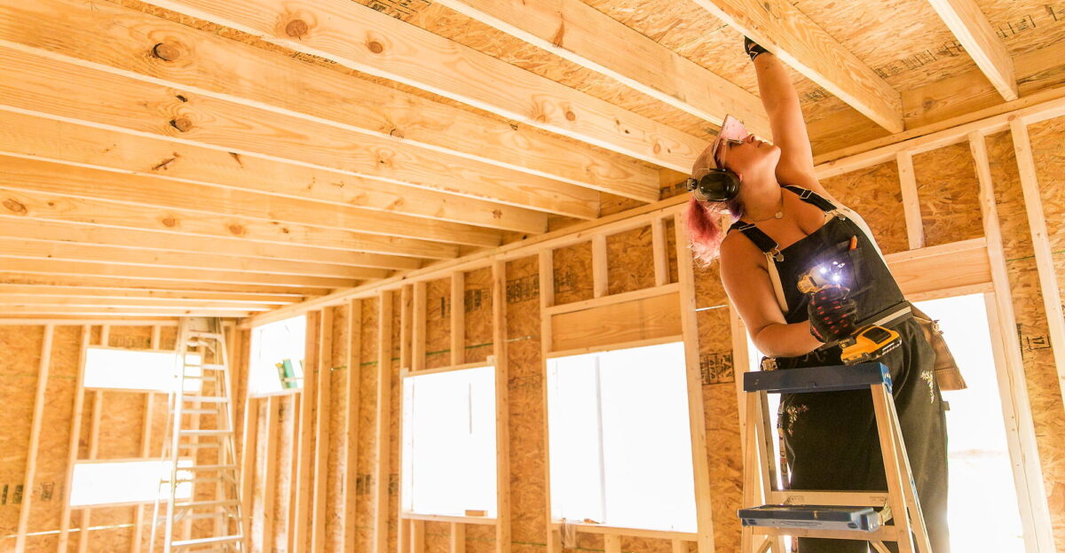 A woman reaches up to check her work inside a Tiny House shell she is constructing as part of a Tiny House Building Workshop at Wild Abundance