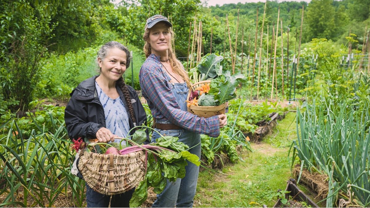 2 women apprentices holding baskets of vegetables they've harvested during a typical day at the 9 month gardening and permaculture apprenticeship program at Wild Abundance