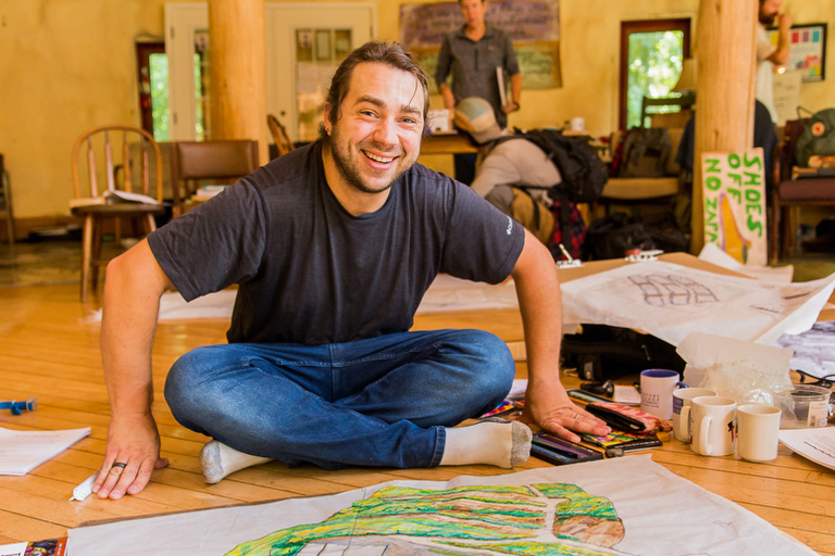 A male permaculture design student smiles up from drawing his final map project for a Permaculture Design Certificate program at Wild Abundance