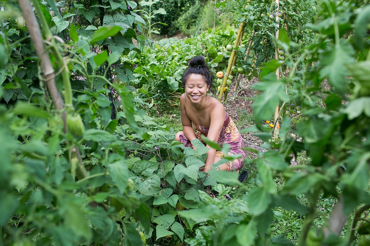 A female apprentice smiles while reaching into a garden bed at Wild Abundance